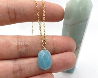 May include: A gold chain necklace with a light blue aquamarine pendant. The pendant is faceted and has a slightly oval shape.