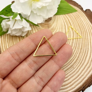 Pode incluir: Dois quadros de metal em forma de triângulo de cor dourada. Os quadros são abertos e têm um acabamento liso e brilhante.