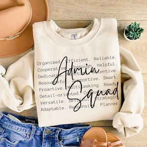 Puede incluir: Sudadera de color crema con las palabras "Admin Squad" en una fuente de escritura negra. La sudadera tiene cuello redondo y mangas largas. Las palabras "Organizado, Eficiente, Confiable" están impresas en negro.