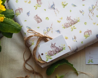 Könnte beinhalten: Ein weißes Geschenkpapier mit einer braunen Kordelschleife und einem Geschenkanhänger. Das Geschenkpapier zeigt ein sich wiederholendes Muster aus Hasen, Vögeln und Blumen. Der Geschenkanhänger zeigt ein Bild einer Hasenfamilie.