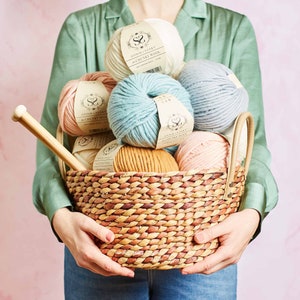 May include: A wicker basket filled with various balls of yarn in shades of white, pink, blue, and brown. The yarn is labelled "Stitch & Story Chunky Wool".