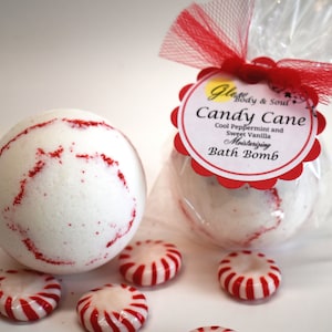 May include: White bath bombs with red accents and peppermint candies. One bath bomb is packaged in cellophane with a red bow and a label that reads "Candy Cane Bath Bomb". The bath bombs are for moisturizing and have a cool peppermint and sweet vanilla scent.