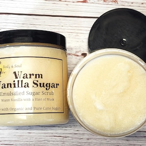 Op de afbeelding: Een glazen pot met warme vanille-suikerscrub. De pot heeft een zwarte deksel en een wit etiket met de tekst "G Body & Soul Glow Warm Vanilla Sugar Emulsified Sugar Scrub Warm Vanilla with a Hint of Musk Made with Organic and Pure Cane Sugars".