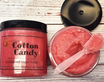 May include: A pink sugar scrub in a glass jar with a black lid. The jar is labeled "Cotton Candy" and "Sweet and Sugary Concoction! Emulsified Sugar Scrub. Made with Organic and Pure Cane Sugars."