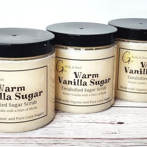Op de afbeelding: Drie glazen potten gevuld met een lichtbruine suiker scrub. Elke pot heeft een zwarte deksel en een wit etiket met de tekst "Warm Vanilla Sugar" en "Emulsified Sugar Scrub". Het etiket bevat ook de tekst "Warm Vanilla with a Hint of Musk" en "Made with Organic and Pure Cane Sugars".