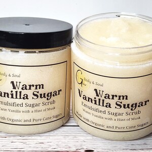 Op de afbeelding: Twee glazen potten met warme vanille-suikerscrub. De potten zijn gelabeld met "Warm Vanilla Sugar" en "Emulsified Sugar Scrub". De scrub is gemaakt met biologische en pure rietsuiker.
