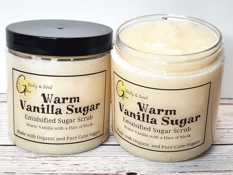 Op de afbeelding: Twee glazen potten met warme vanille-suikerscrub. De potten zijn gelabeld met "Warm Vanilla Sugar" en "Emulsified Sugar Scrub". De scrub is gemaakt met biologische en pure rietsuiker.