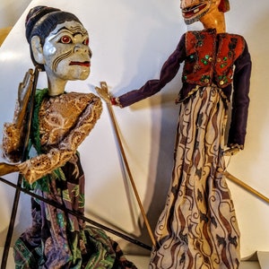 Peut inclure: Deux marionnettes d'ombres indonésiennes traditionnelles, l'une avec un visage blanc et des yeux rouges, l'autre avec un visage brun et une coiffe bleu et blanc. Les deux marionnettes portent des vêtements à motifs élaborés.