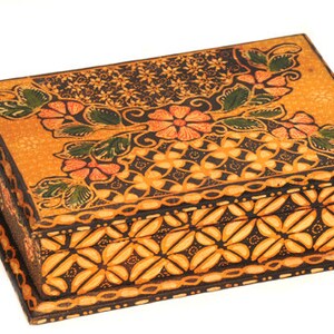 May include: A wooden box with a decorative floral pattern in shades of orange, brown, and green. The box has a hinged lid and a detailed geometric pattern on the bottom.