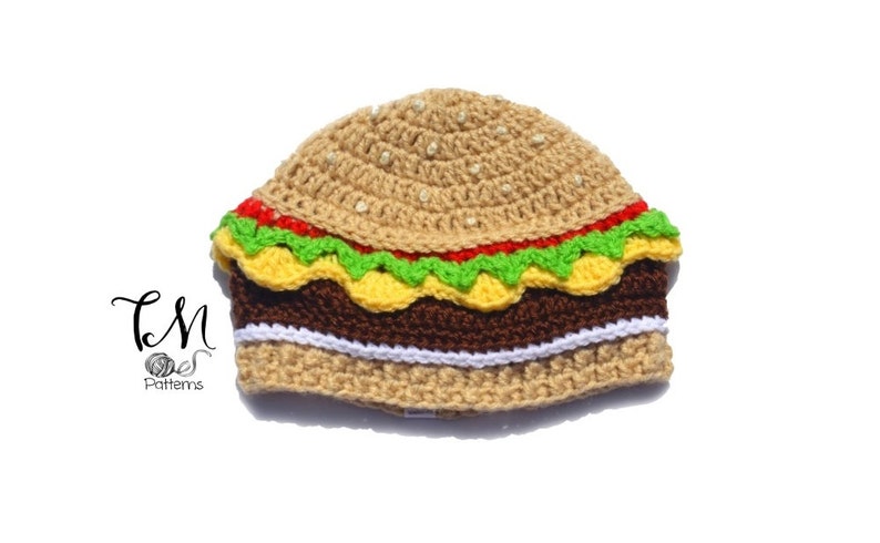 May include: A crocheted hamburger hat with a brown bun, yellow cheese, green lettuce, and red tomato.