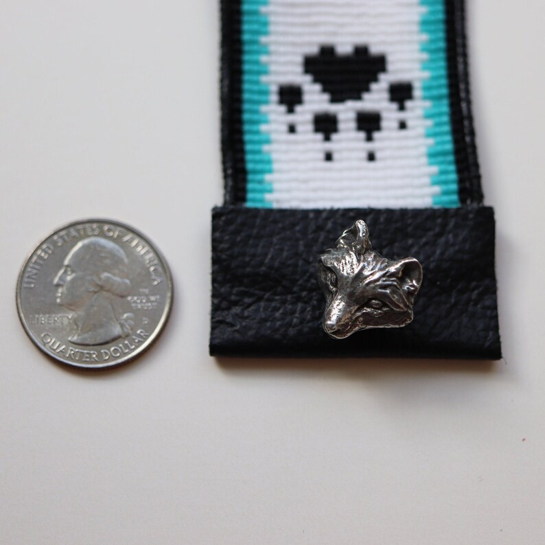 May include: A silver fox head charm with a black leather strap and a turquoise and white patterned fabric strap.