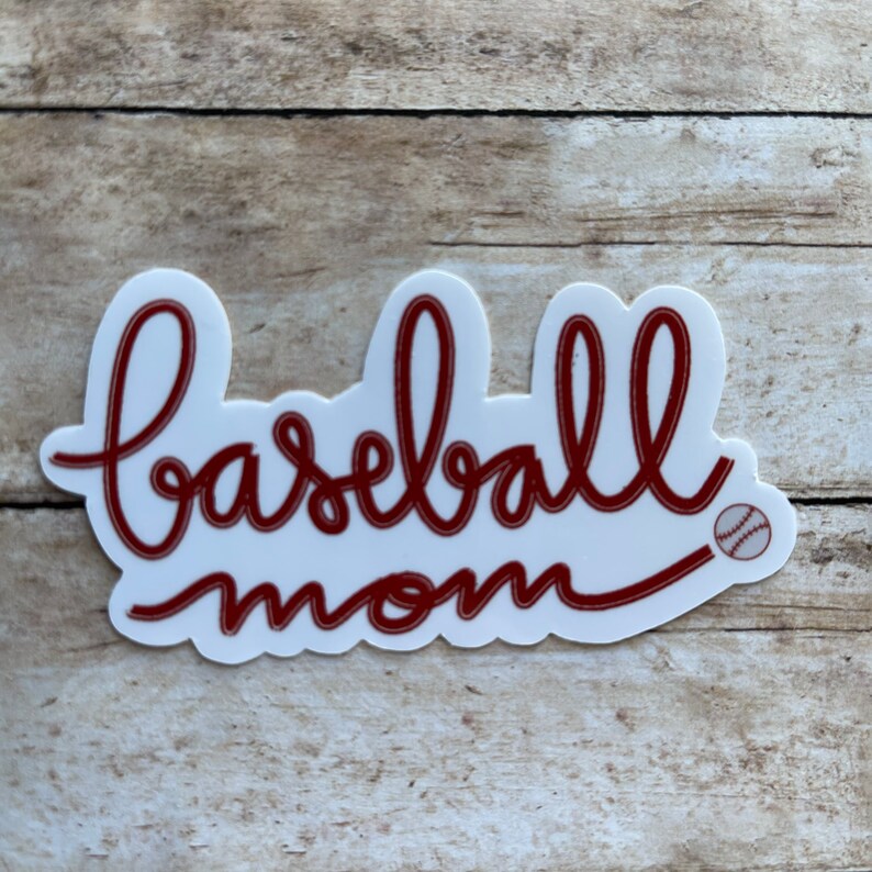 May include: White sticker with red cursive text that reads "baseball mom" with a small baseball graphic to the right of the text.