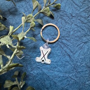 May include: A silver key chain with a clear plastic charm featuring a pair of crossed hockey sticks.