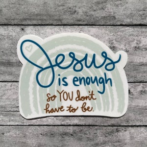 Puede incluir: Una pegatina blanca con un dise&ntilde;o azul y marr&oacute;n. La pegatina presenta un arco&iacute;ris con el texto "Jes&uacute;s es suficiente para que t&uacute; no tengas que serlo."