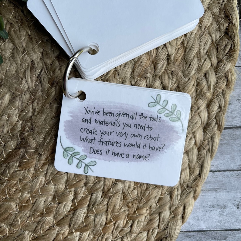 May include: A white card with green leaves and a watercolor background. The card has the text "You've been given all the tools and materials you need to create your very own robot. What features would it have? Does it have a name?"