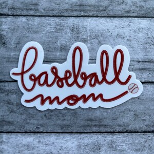 May include: White sticker with red cursive text that says "baseball mom" with a small red baseball graphic.