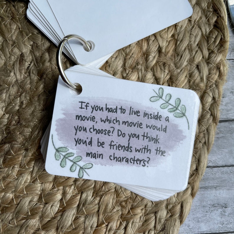 May include: A white card with a watercolor background and green leaves drawn on it. The card has the text "If you had to live inside a movie, which movie would you choose? Do you think you'd be friends with the main characters?"