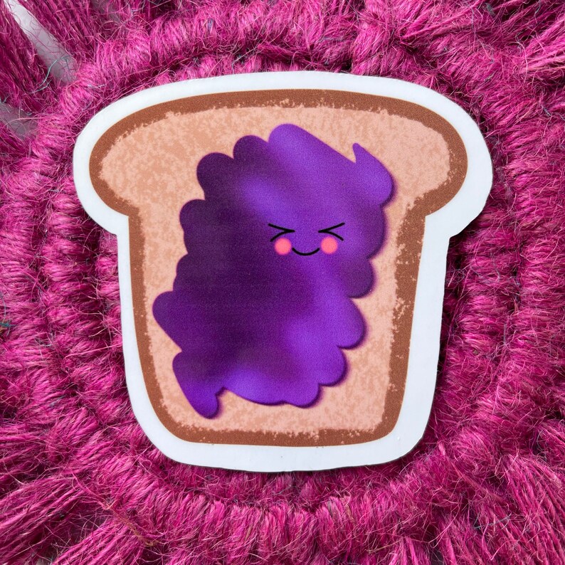 May include: A cartoon sticker of a slice of bread with purple jam on top. The jam has a smiling face and is shaped like a blob.