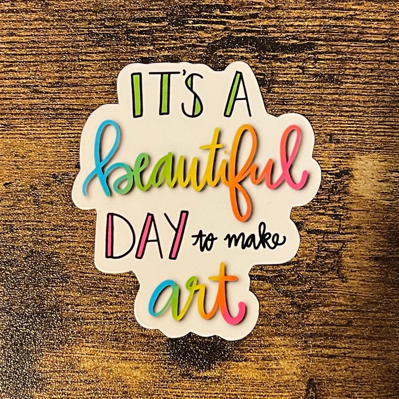 May include: A colorful sticker with the text "It's a beautiful day to make art". The text is written in a whimsical font and is surrounded by a white background.