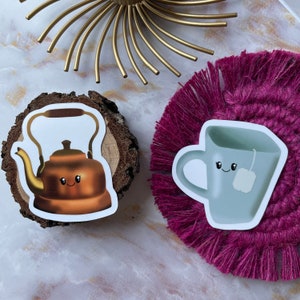 May include: Two cartoon stickers, a brown teapot and a white teacup, both with smiling faces. The teapot is on a wooden surface and the teacup is on a pink and purple fuzzy surface.