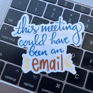Pode incluir: Um adesivo branco com texto azul e marrom que diz "Esta reuni&atilde;o poderia ter sido um e-mail". O adesivo est&aacute; colocado em um teclado de laptop prateado.