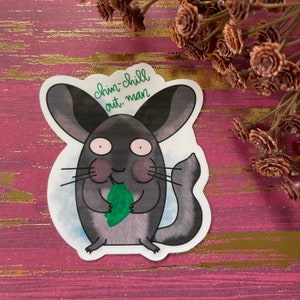 May include: A die-cut sticker featuring a cartoon chinchilla with gray fur, pink cheeks, and a green leaf. The sticker has the text "chin-chill out, man" in green script. The background is a watercolor wash.