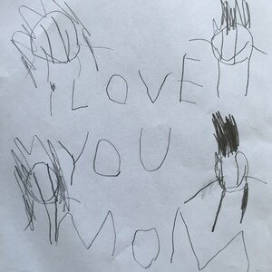 May include: A child's drawing on white paper. The drawing includes the words "I LOVE YOU MOM" in large, uneven letters. There are also several stick figures and flower-like shapes drawn in black marker. The overall style is simple and childlike.