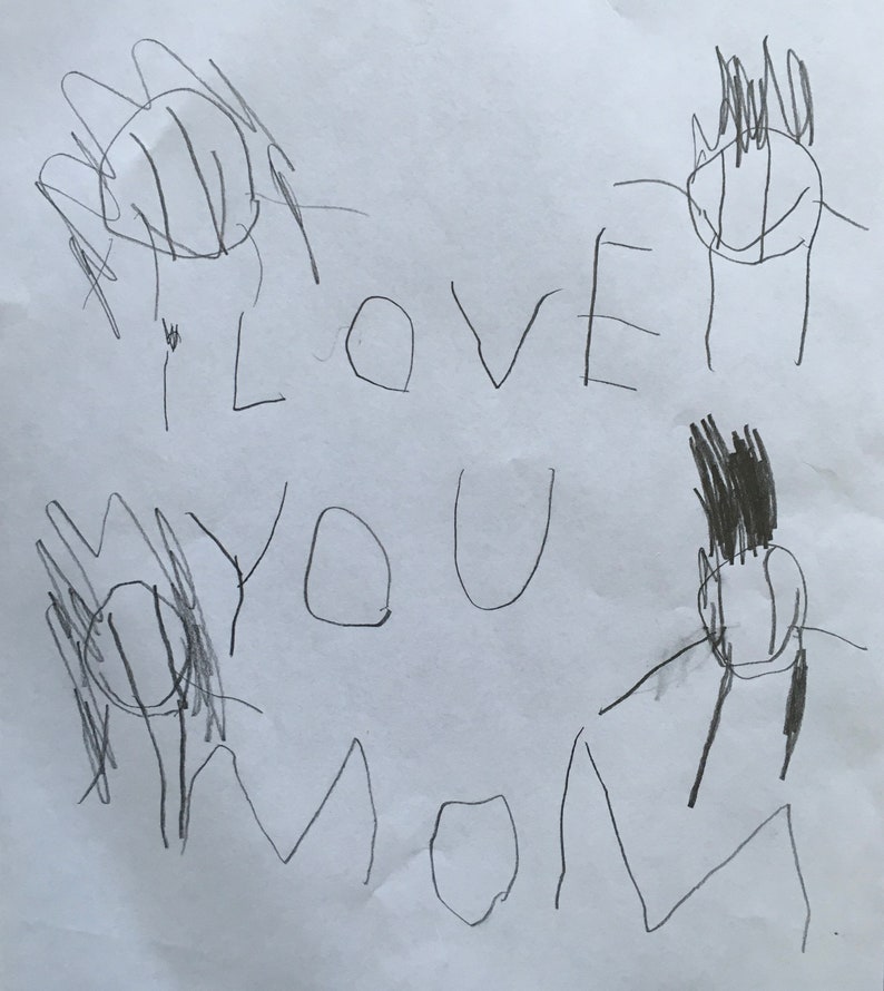 May include: A child's drawing on white paper. The drawing includes the words "I LOVE YOU MOM" in large, uneven letters. There are also several stick figures and flower-like shapes drawn in black marker. The overall style is simple and childlike.