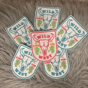 May include: Six embroidered patches with a skull and crossbones design. The patches are white with blue, green, pink, and yellow embroidery. The text on the patches reads "Wild Like The West".