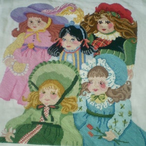 May include: Five embroidered dolls with different coloured dresses and hats. The dolls are all smiling and have brown hair. The dolls are arranged in a row, with the tallest doll at the back and the shortest doll at the front.