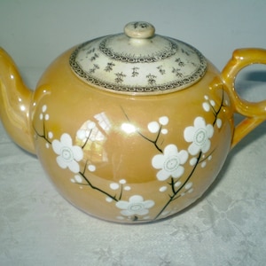 May include: A yellow teapot with a white floral design and a lid with a brown and white pattern.