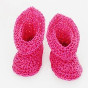 Puede incluir: Un par de botitas de bebé de crochet rosa. Las botitas están hechas con un hilo suave y texturizado y tienen un diseño simple y clásico.