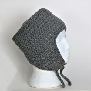 May include: Grey crocheted hat with ear flaps and ties. The hat is on a white mannequin head.