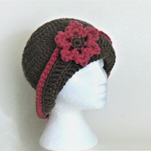 May include: A brown crocheted cloche hat with a pink crocheted flower accent.