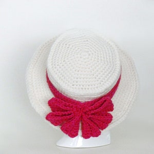 May include: A white crocheted hat with a wide brim and a pink crocheted bow.