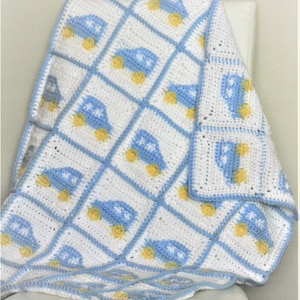 May include: A blue and white crocheted baby blanket with a pattern of cars. The blanket is folded and draped over a white chair.