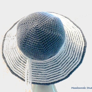 May include: A crocheted sun hat with a wide brim. The hat is made with white and gray yarn and has a striped pattern. The hat is turned inside out, showing the gray yarn on the inside.
