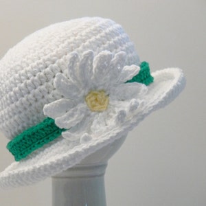 Puede incluir: Sombrero de sol blanco de ganchillo con una cinta verde y una flor de margarita blanca de ganchillo.