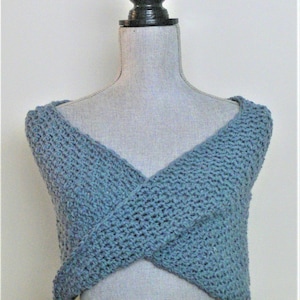 Puede incluir: Un chal de ganchillo azul con un diseño de cuello en V, exhibido en un maniquí.