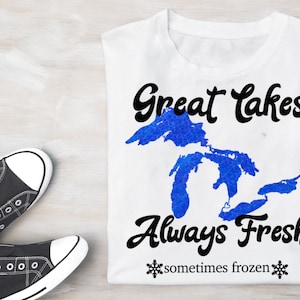 May include: White t-shirt with a blue outline of the Great Lakes and the text "Great Lakes Always Fresh sometimes frozen" in black.