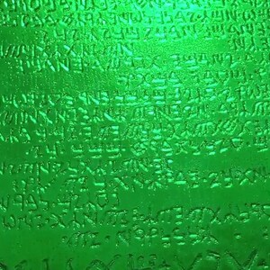 May include: A close-up of a green glass bottle with a textured surface. The bottle is covered in a pattern of raised letters and symbols.
