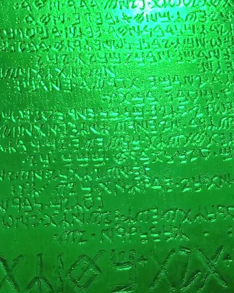 May include: A close-up of a green glass bottle with a textured surface. The bottle is covered in a pattern of raised letters and symbols.