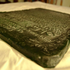 May include: A dark green, rectangular, glass slab with a textured surface. The slab has a rough, uneven edge.
