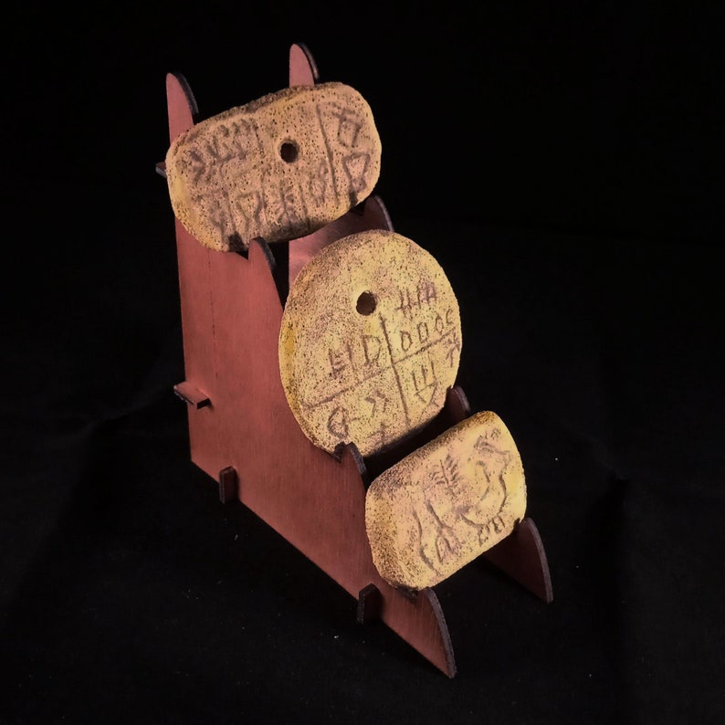May include: Three clay tokens with cuneiform script on a wooden stand. The tokens are light brown and have holes in the center. The stand is a dark brown color.