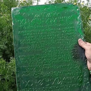 A reproduction of the Emerald Tablet appears on screen, held in one hand to clearly show the proportions (30x40 cm). Image taken in daylight.