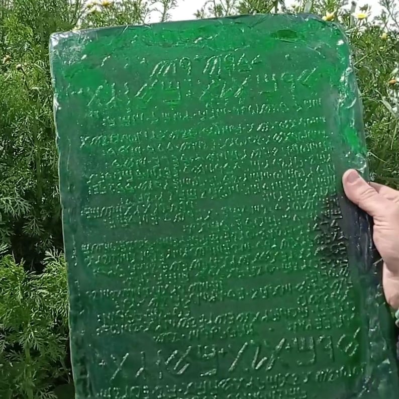A reproduction of the Emerald Tablet appears on screen, held in one hand to clearly show the proportions (30x40 cm). Image taken in daylight.