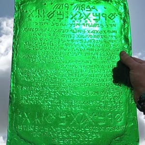 May include: A green glass plaque with an inscription of an unknown language. The inscription is carved into the glass and appears to be a long text.