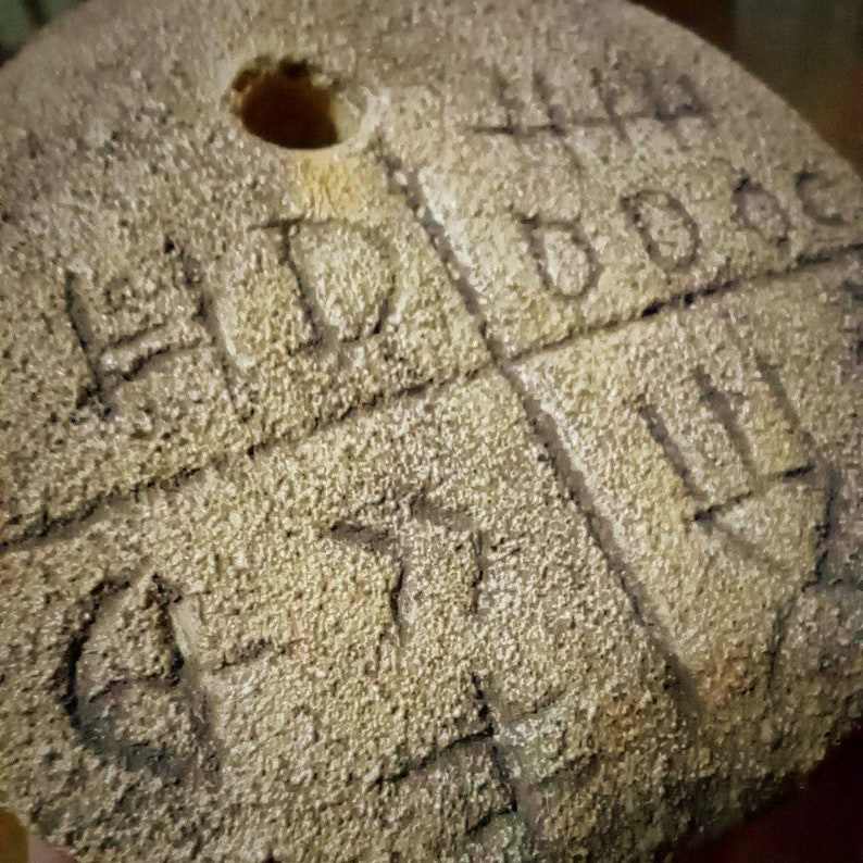 May include: A close-up of a wooden disc with a hole in the center. The disc is covered in a rough, textured surface and has various markings carved into it.
