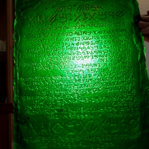 May include: A green glass plaque with an inscription in an unknown language. The inscription is carved into the glass and appears to be ancient.