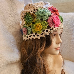 May include: A crocheted hat with a floral design in shades of green, pink, yellow, and red. The hat is made with a beige yarn and has a delicate lace pattern.